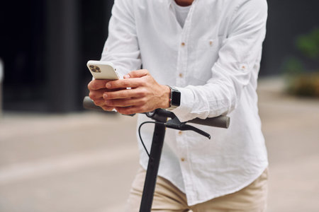 Close up view. Stylish man is with his scooter outdoors at daytime.