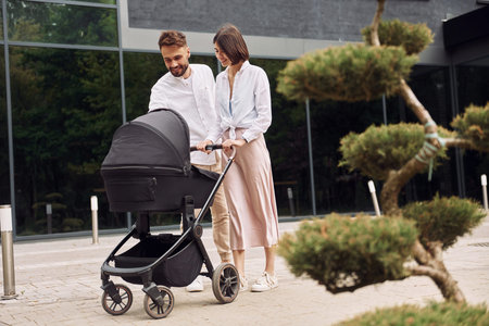 Conception of love. Young parents having a walk with baby carriage outdoors.