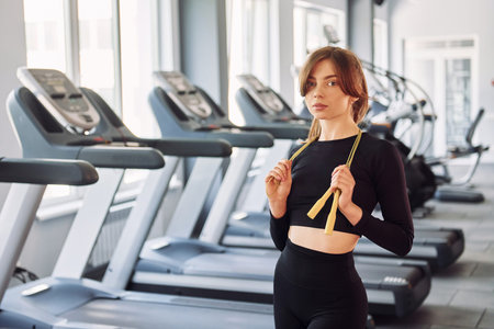 Holding jump rope. Young beautiful woman in sportive clothes have fitness day in the gym.
