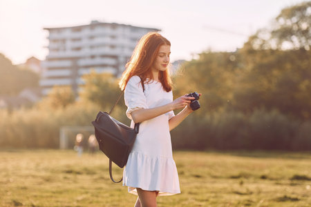 Professional camera in hands. Young girl is on the field at sunny daytime having nice weekend.