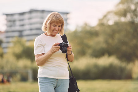 Photographer with a camera. Senior woman having nice weekend outdoors on the field at sunny day.