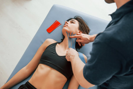Laying down on the table. Woman visiting physiologist that putting kinesio tape on the skin.