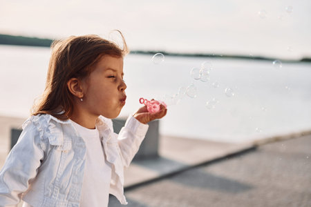 Playing with bubbles, Little cute girl having fun outdoors at summer near the lake.