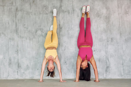 Standing on the hands by leaning on the wall. Beautiful women in sportive clothes is indoors in the...