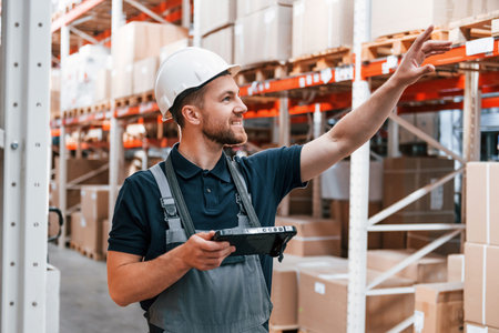 Walking near the shelves. Employee in uniform is working in the storage at daytime.