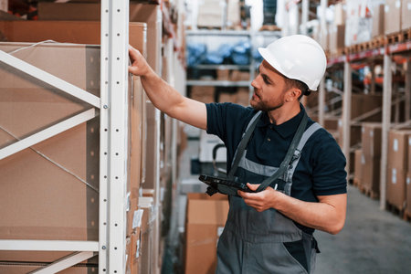 Checking the box. Employee in uniform is working in the storage at daytime.