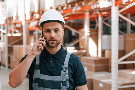 Talking by phone. Employee in uniform is working in the storage at daytime.