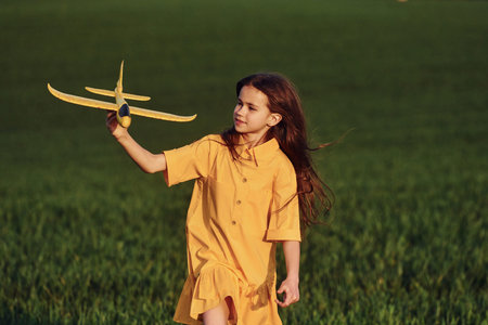 Running forward with toy plane. Happy girl have a walk outdoors on the field at summer.