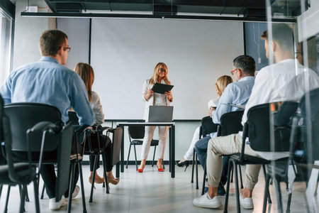 Woman with notepad in hands doing master class. Group of professional business people is in the...