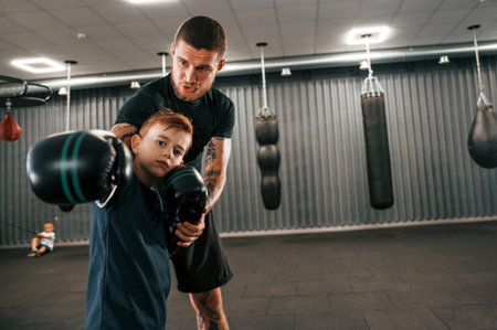 Giving advices. Coach is teaching the boy box techniques indoors.