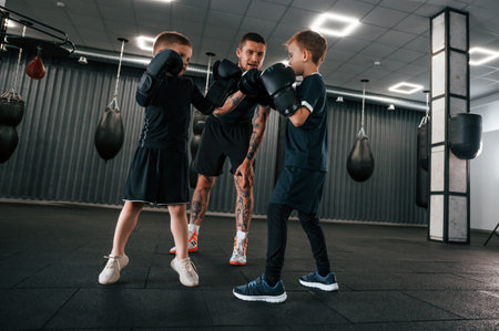 Having fun by practicing. Young tattooed coach teaching the kids boxing techniques.