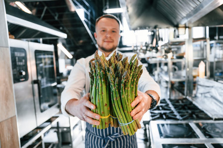 Man holding asparagus. Chef is on the kitchen preparing food.の写真素材