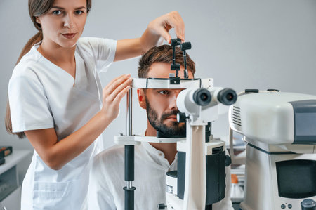 Man's vision checked by female doctor in the clinic by using special optometrist device.