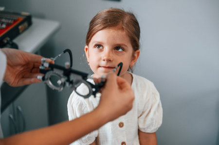 In special device with lenses. Little girl have their vision checking in the clinic by help of the...