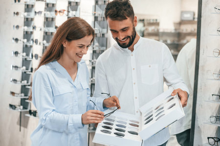 Holding replaceble lenses. Man and woman in the glasses store. Helping to choose product.