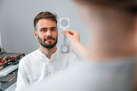 Holding tool. Man's vision checked by female doctor in the clinic by using special optometrist...
