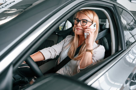 Driving new automobile. Woman in white formal clothes is in the car dealership.
