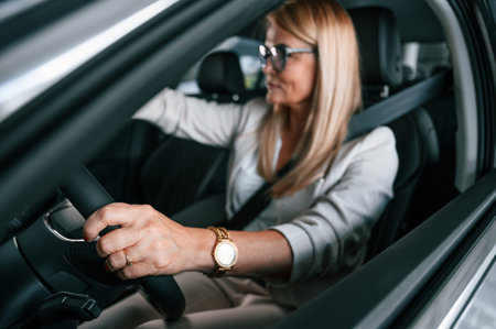 Sitting inside of the new automobile. Woman in white formal clothes is in the car dealership.