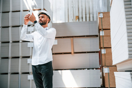 Using phone. Storage worker is in the warehouse with bunch of products.