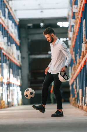 Kicking soccer ball. Storage worker is in the warehouse with bunch of products.