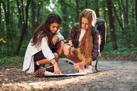 Looking at the map hat is on the ground. Two girls is in the forest having a leisure activity.