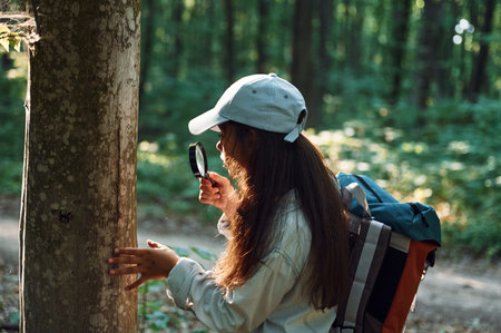 With magnifying glass. Girl is in the forest at summer day time discovering new places.