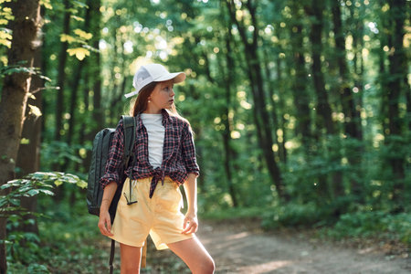 Standing and looking at nature. Girl is in the forest at summer day time discovering new places.