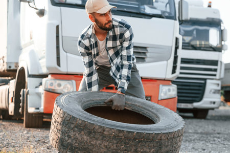 With broken tire. Young truck driver is with his vehicle at daytime.
