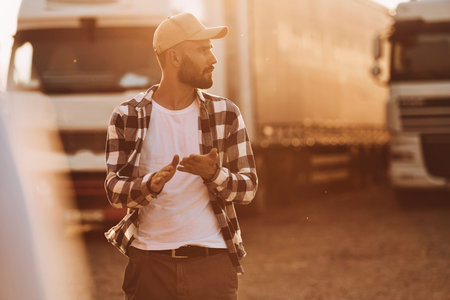 Illuminated by beautiful sunlight. Young truck driver is with his vehicle at daytime.