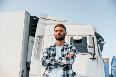 With arms crossed. Young truck driver is with his vehicle at daytime.