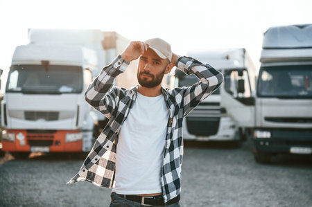 Front view. In cap. Young truck driver is with his vehicle at daytime.の写真素材