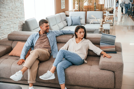 Sitting and relaxing. Couple choosing the sofa and bed in the store.