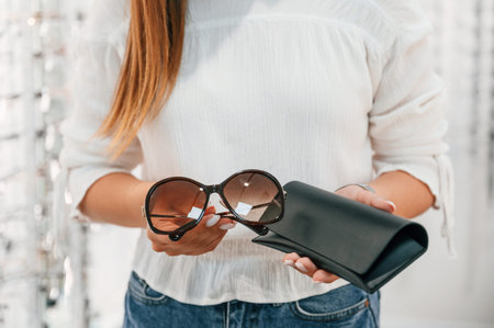 Brown colored lenses and black case. Woman holding glasses in hands in the store. Close up view.