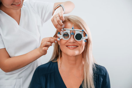 Wearing glasses. Woman's vision is tested by clinic worker that using special device.
