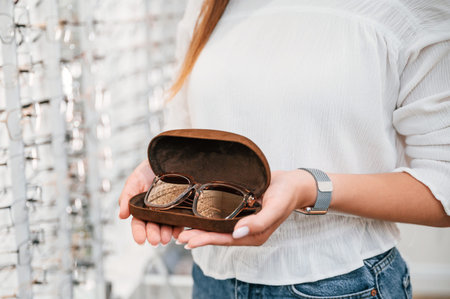 In brown colored case. Woman holding glasses in hands in the store. Close up view.