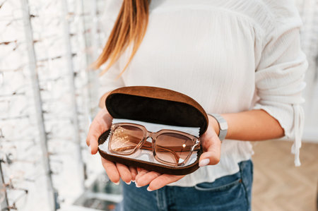 In brown colored case. Woman holding glasses in hands in the store. Close up view.の写真素材