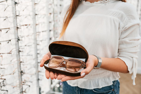 In brown colored case. Woman holding glasses in hands in the store. Close up view.の写真素材