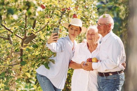 Woman is making selfie. Daughter is with her senior mother and father is in the garden.