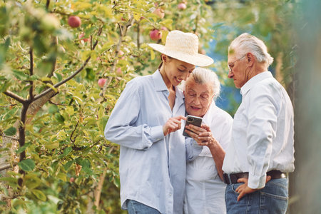 Woman showing something on the smartphone. Daughter is with her senior mother and father is in the garden.の写真素材
