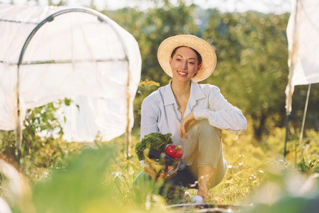 Sitting on the ground. Young cheerful woman is in the garden at daytime.