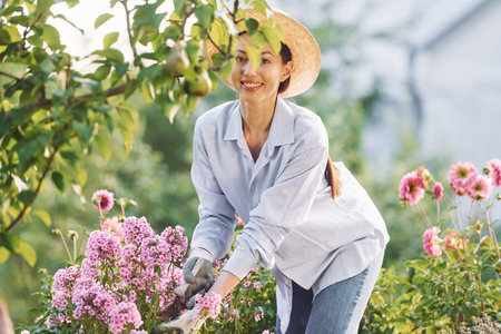 Taking care of flowers. Young cheerful woman is in the garden at daytime.