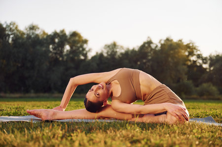 Stretching exercises. Young woman in yoga clothes is outdoors on the field.の写真素材