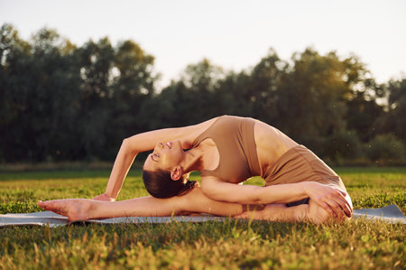 Stretching exercises. Young woman in yoga clothes is outdoors on the field.の写真素材