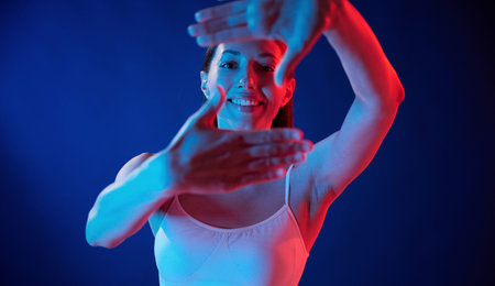Doing gestures by the hands. Young woman in underwear is in the studio with neon lights.