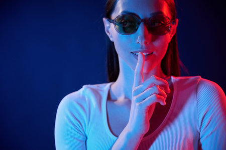 Showing silence gesture. Portrait of young woman that is indoors in neon lighting.