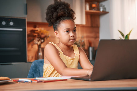 Using laptop. Cute black girl in casual clothes is at home at daytime.