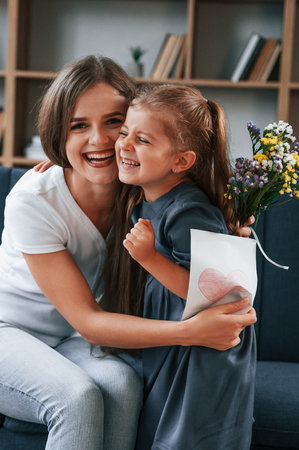 Conception of mother's day. Giving gift. Young woman with her daughter is together at apartment.の写真素材