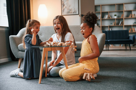 Having fun. A young woman with two girls is playing a wooden tower game indoors together.