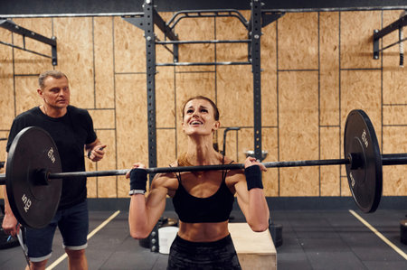 Doing squats. Woman is lifting barbell in the gym.