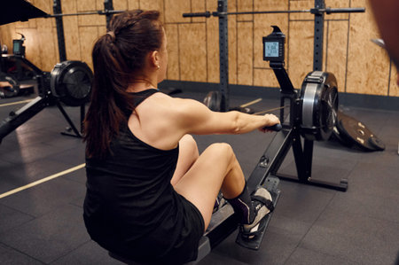 Sportive woman doing exercises on rowing machine in the gym.